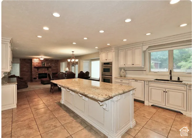 Kitchen featuring a central island with a stone countertop, off-white cabinetry with decorative corbels, built-in double wall ovens, recessed lighting, and tile flooring