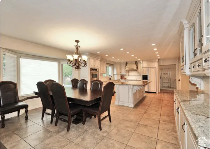 Kitchen featuring cream-toned cabinetry, a central island with countertop seating, stone-finish countertops, tile flooring, and a multi-arm chandelier
