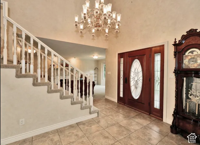 Foyer entry featuring a multi-tiered crystal chandelier, wood door with decorative glass inlay, tile flooring, and a staircase with a white balustrade