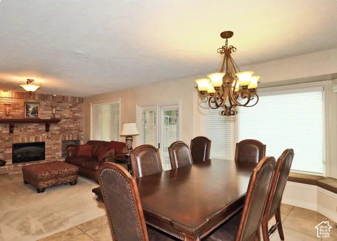 Full-height brick masonry fireplace featuring a wood mantel, multi-light decorative chandelier, large-format tile flooring, and integrated window bench seating