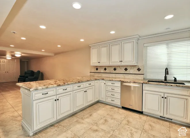 Kitchen featuring custom white cabinetry, stone countertops, stone tile backsplash with decorative accents, stainless steel dishwasher, and recessed lighting