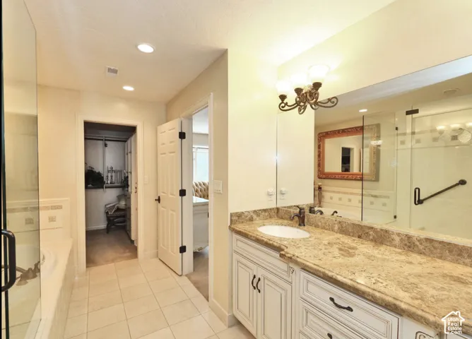 Bathroom featuring a white vanity with stone-surfaced countertop, integrated oval sink, full-width vanity mirror, tile flooring, and glass-enclosed shower