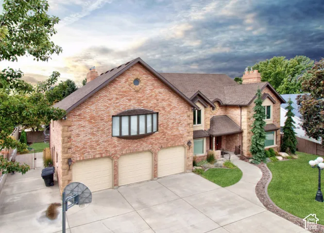 Two-story brick exterior featuring a three-car garage, expansive concrete driveway, arched entryway, and bay window