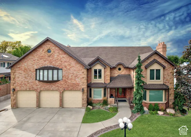Multi-level exterior featuring a brick facade, three-car garage, multiple bay windows, and a structured roofline with accent dormers