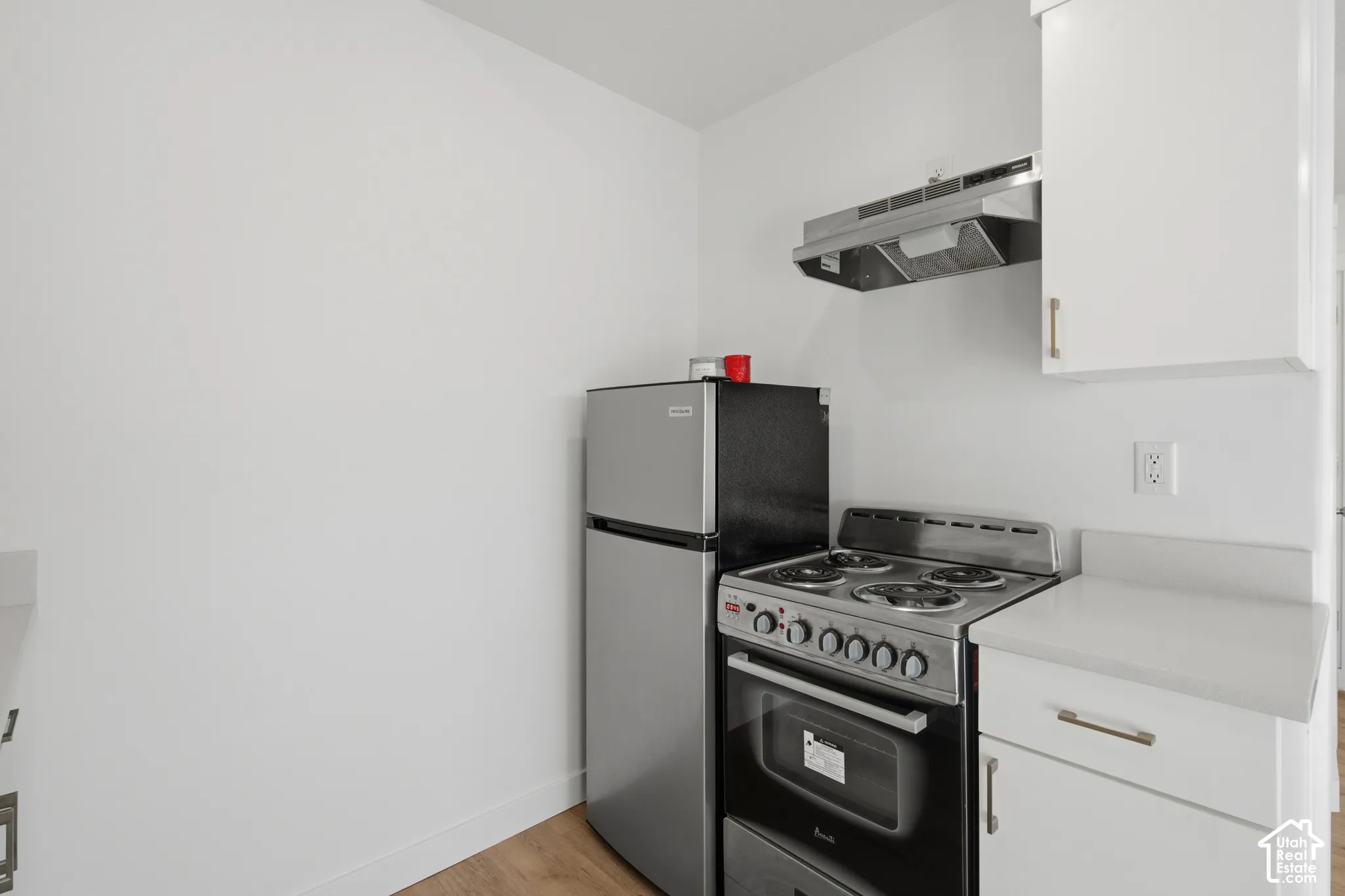 Compact kitchen area featuring white cabinetry, solid-surface countertops, a stainless steel gas range, a stainless steel refrigerator, and a wall-mounted stainless steel exhaust hood