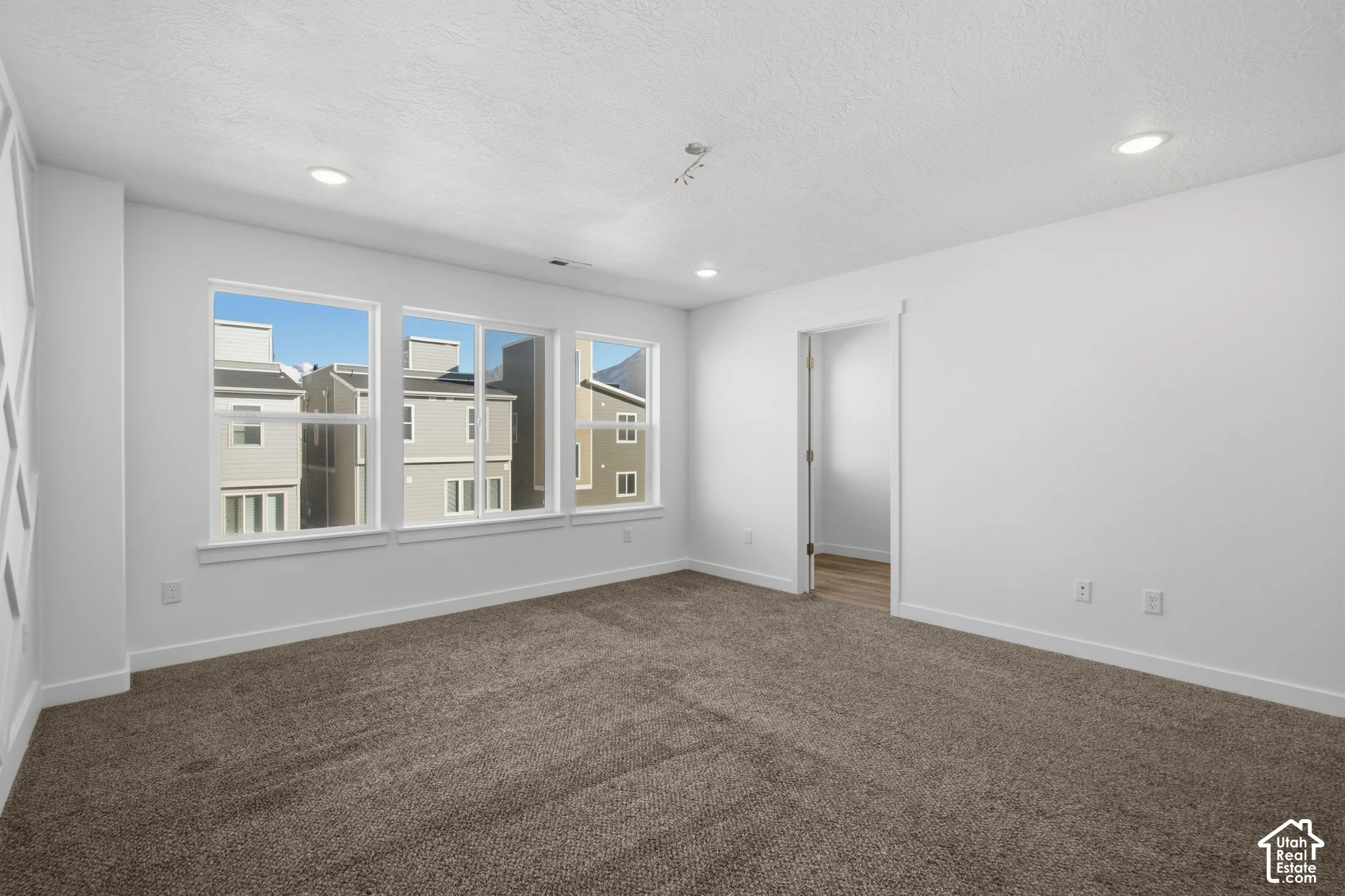 Neutral-toned interior room featuring wall-to-wall carpeting, recessed ceiling lighting, and a triple-window configuration with white trim
