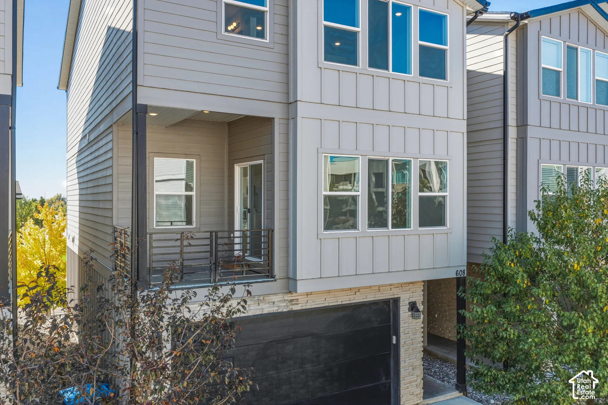 Multi-story exterior featuring composite siding, board and batten detailing, a stone veneer base, metal balcony railing, and a multi-car garage