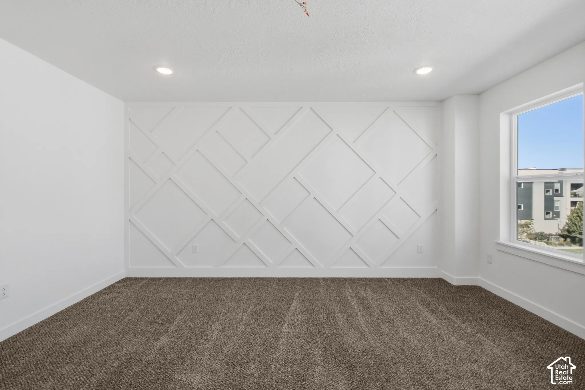 Geometric wall millwork, neutral carpeting, recessed ceiling lighting, and natural light from a single-pane window