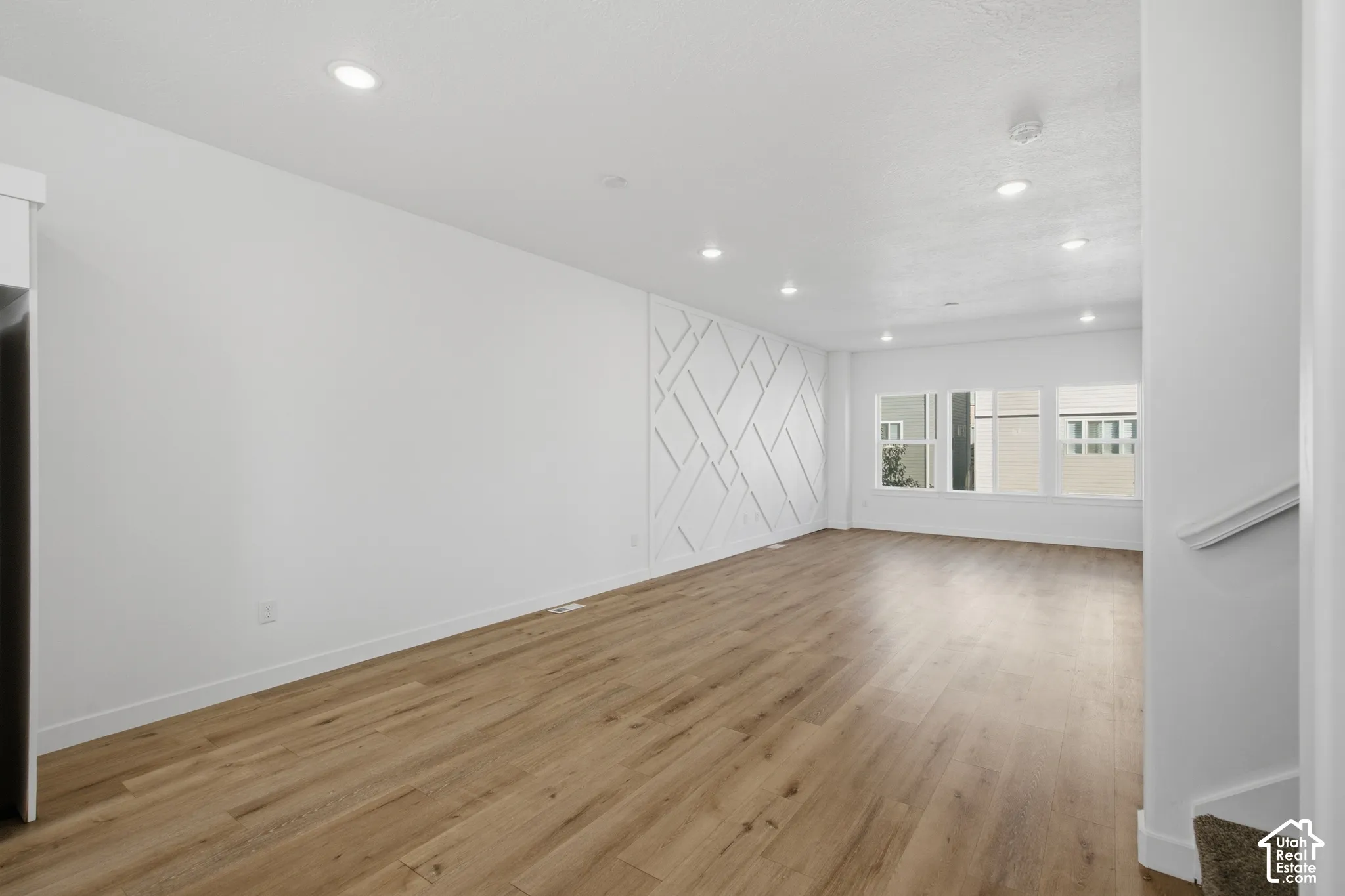 Open-concept interior featuring wood-finish flooring, recessed lighting, and a geometric accent wall