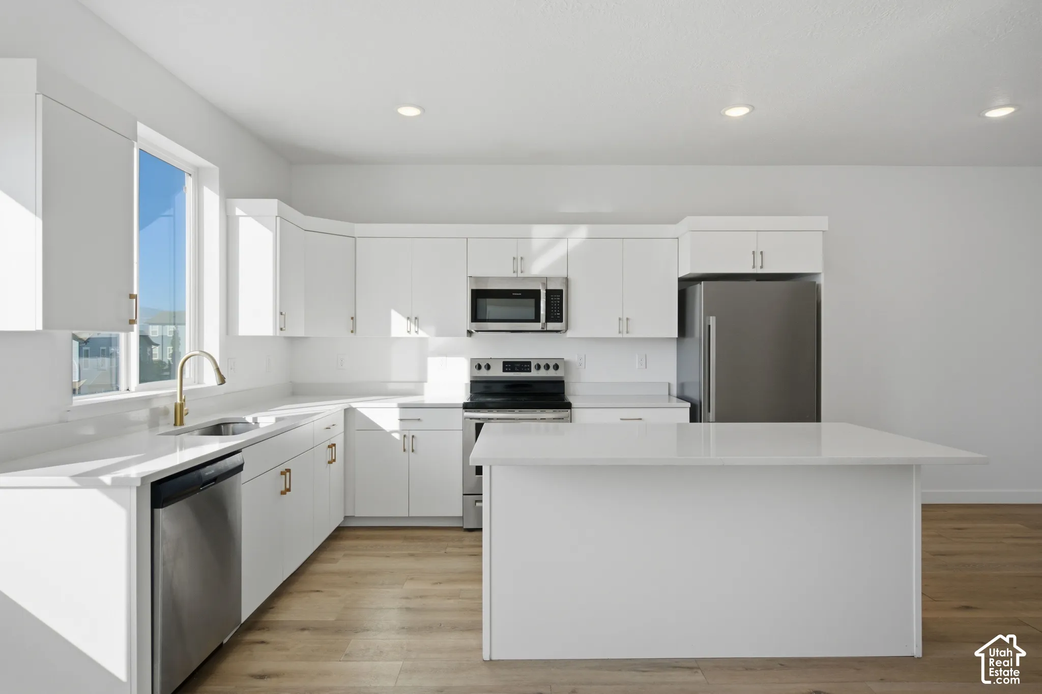 Kitchen featuring white cabinetry, quartz countertops, wood-finish flooring, a central island, and stainless steel appliances