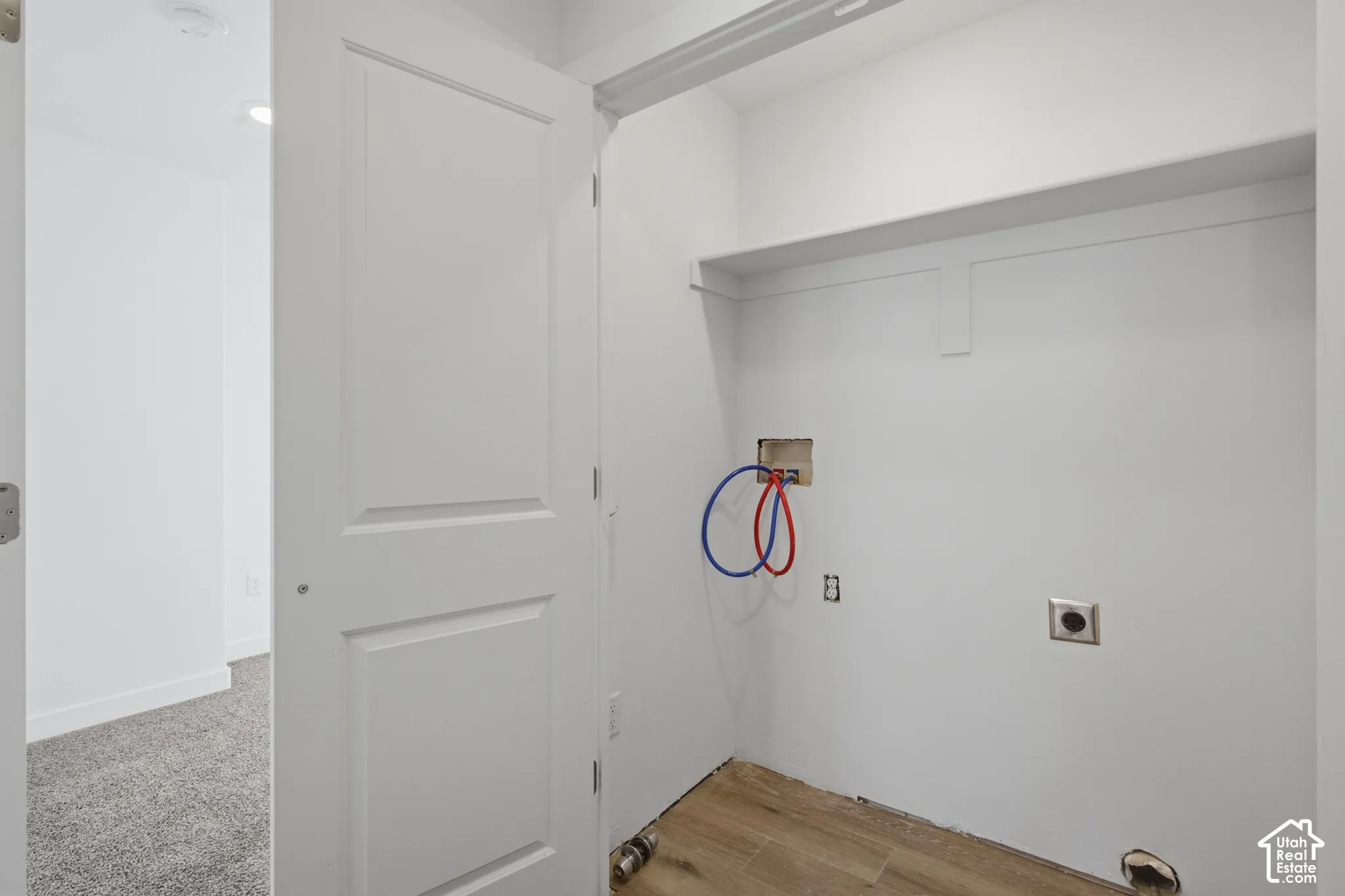 Utility alcove featuring wood-finish flooring, built-in shelving, and dedicated water and electrical hookups