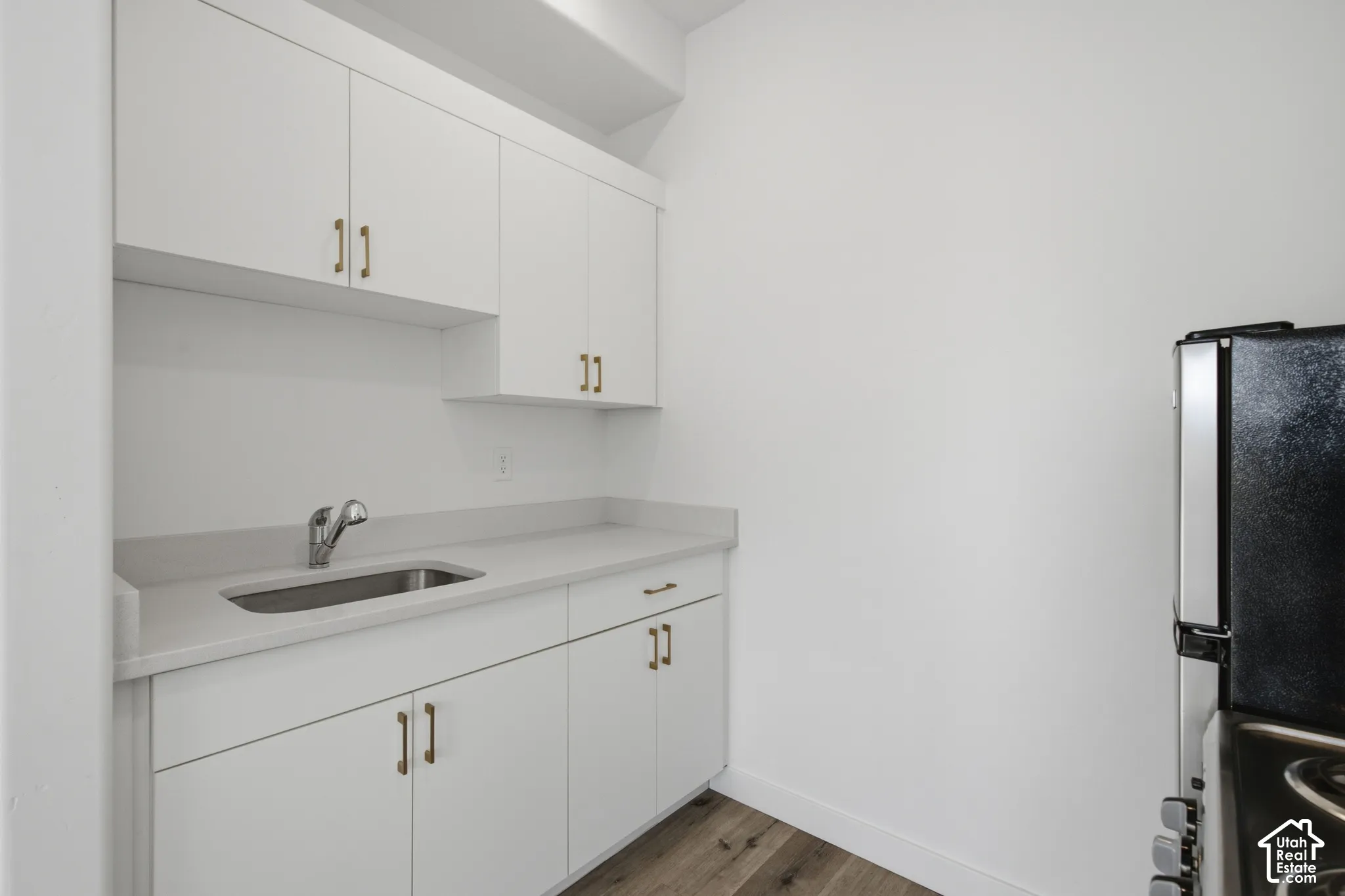 Utility space featuring white cabinetry with metallic pulls, stone-composite countertops, an undermount stainless steel sink, and wood-finish flooring