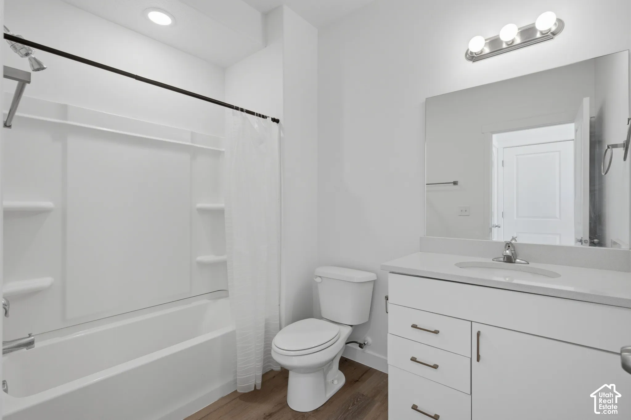 Bathroom featuring a white vanity with integrated countertop sink, wood-finish flooring, a tub-shower combination with built-in shelving, and polished chrome hardware