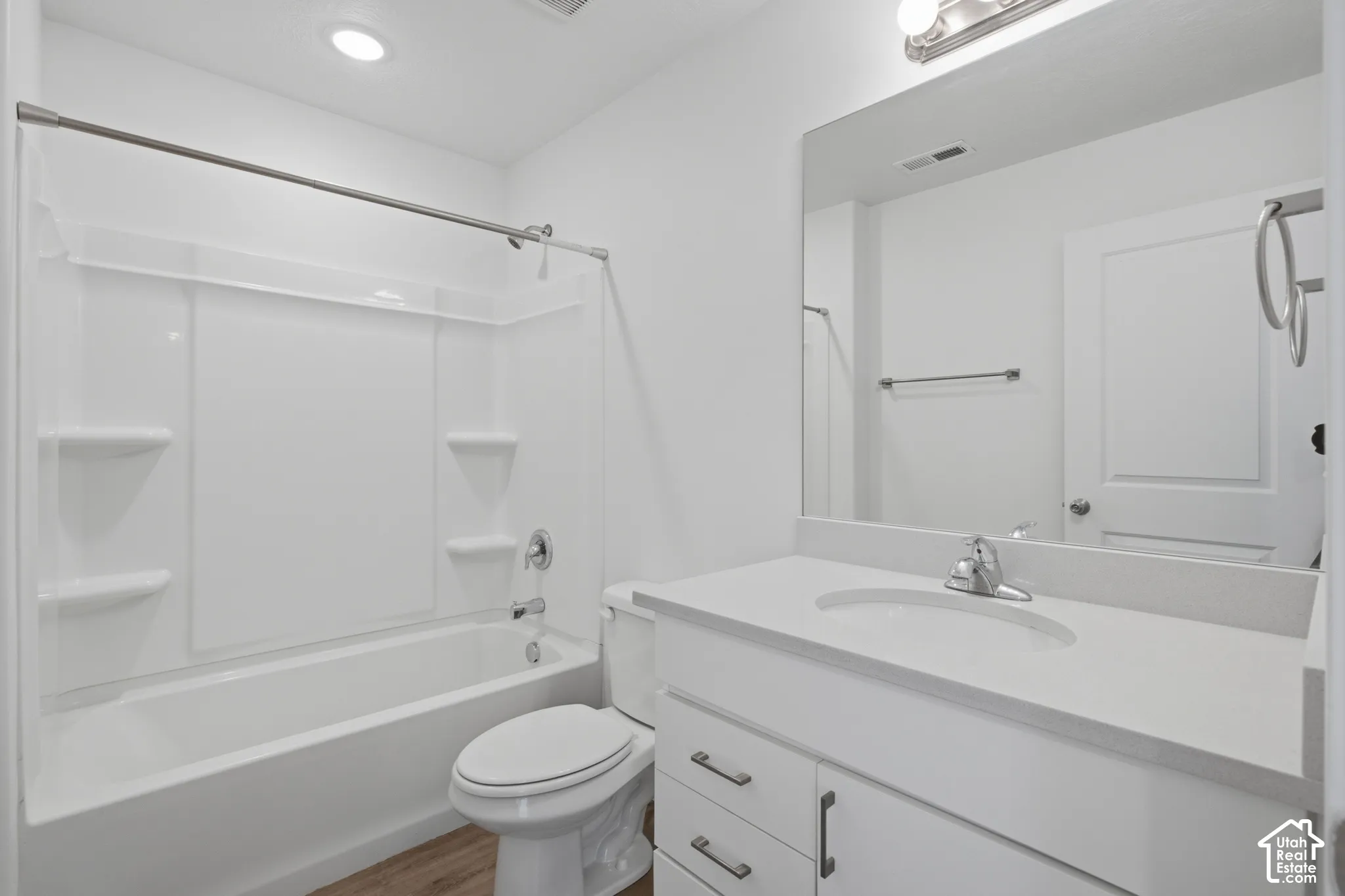 Bathroom featuring a white vanity with a composite countertop, undermount sink, acrylic tub and shower surround with integrated shelving, and a large wall-mounted mirror