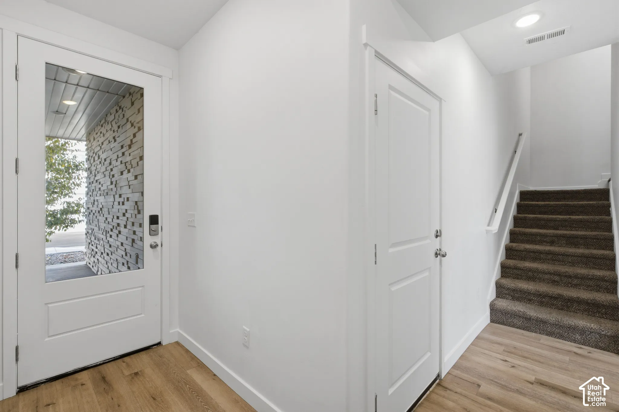 Entryway featuring a solid door with glass pane, recessed ceiling lighting, wood-finish flooring, and carpeted stairs with a white handrail