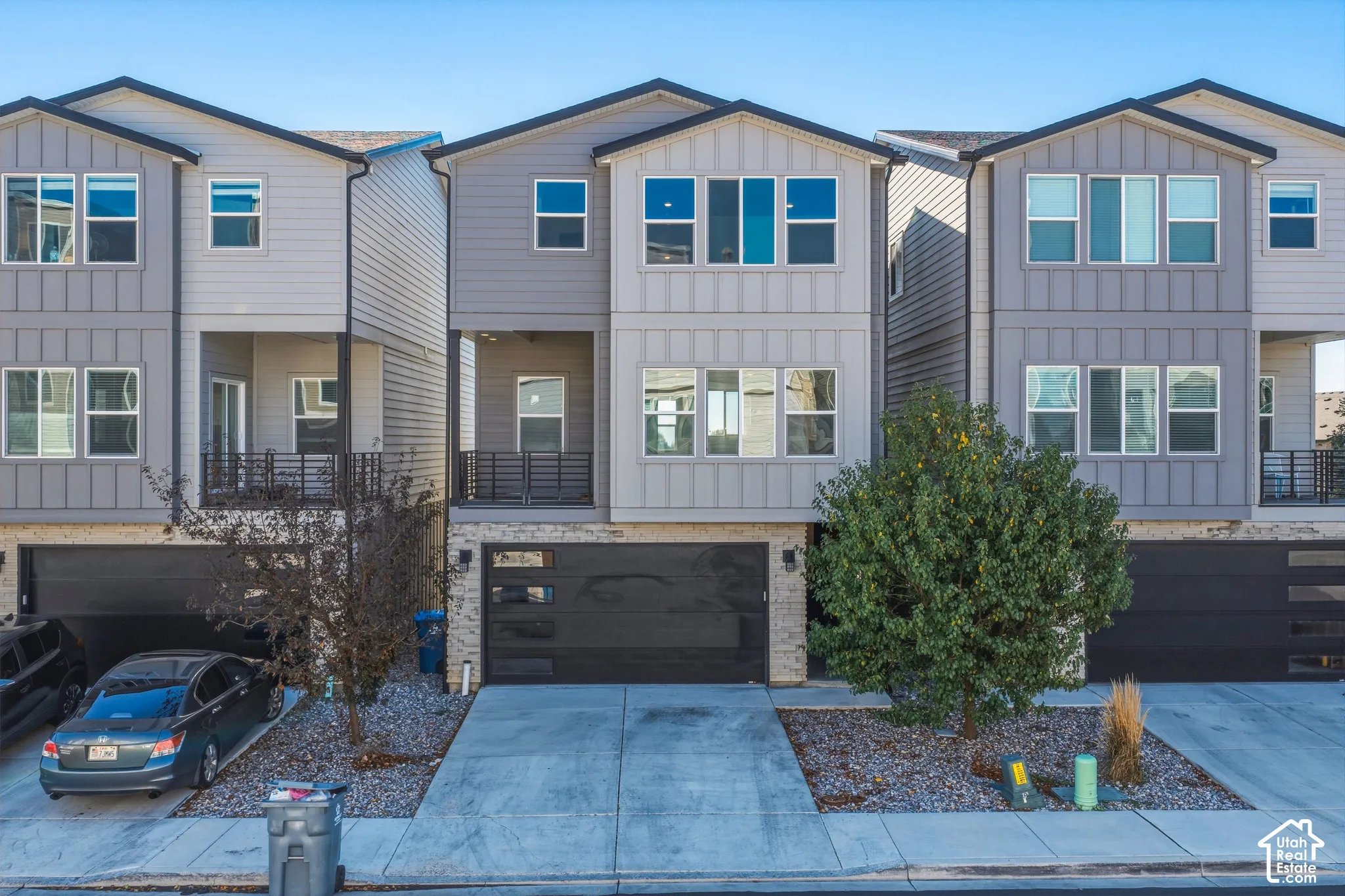 Contemporary multi-level exterior featuring vertical siding, stone masonry base, recessed balcony with metal railing, and an attached multi-panel garage door with horizontal glass inserts