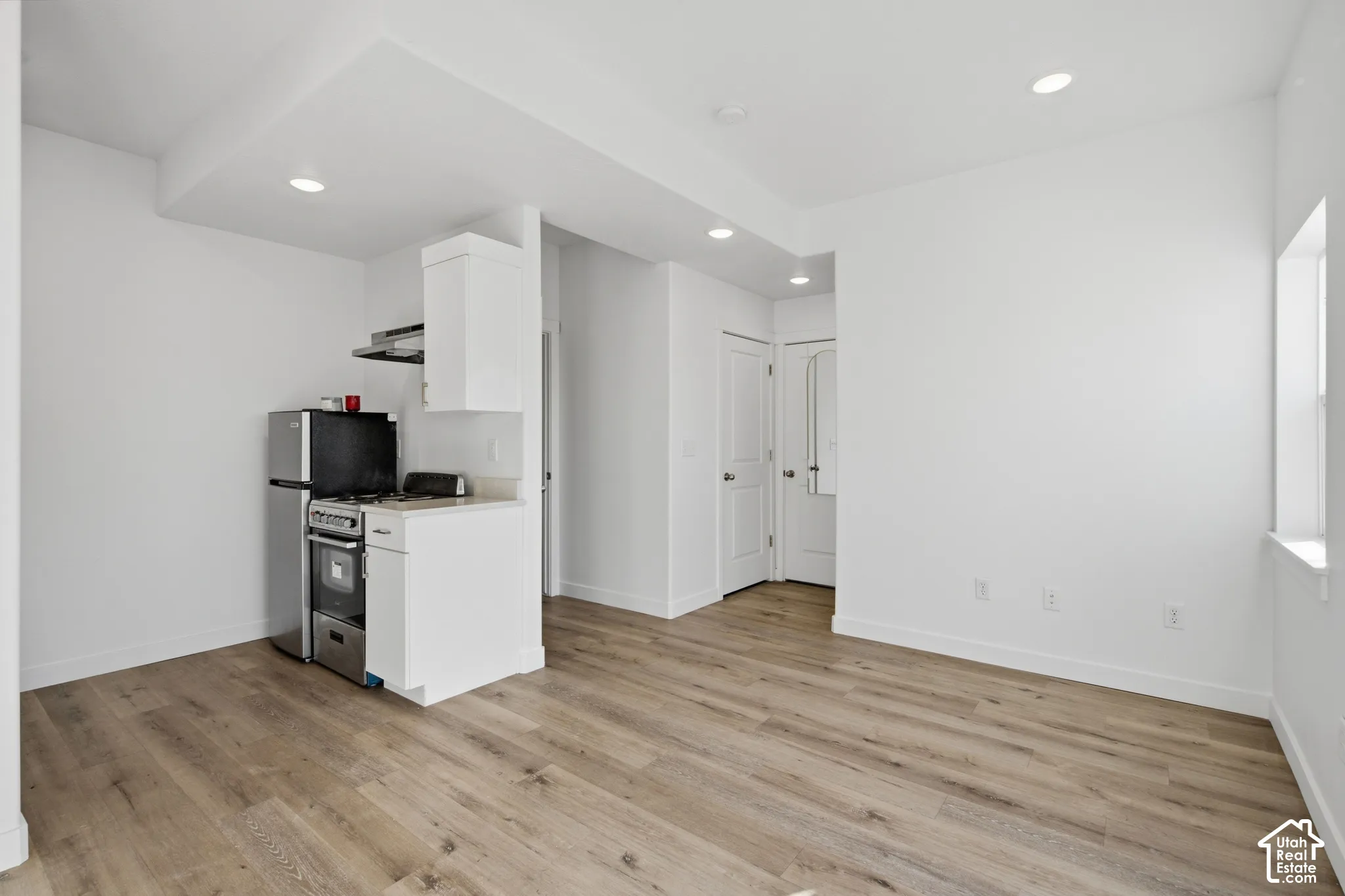Wood-finish flooring, recessed lighting, white cabinetry, and stainless steel kitchen appliances