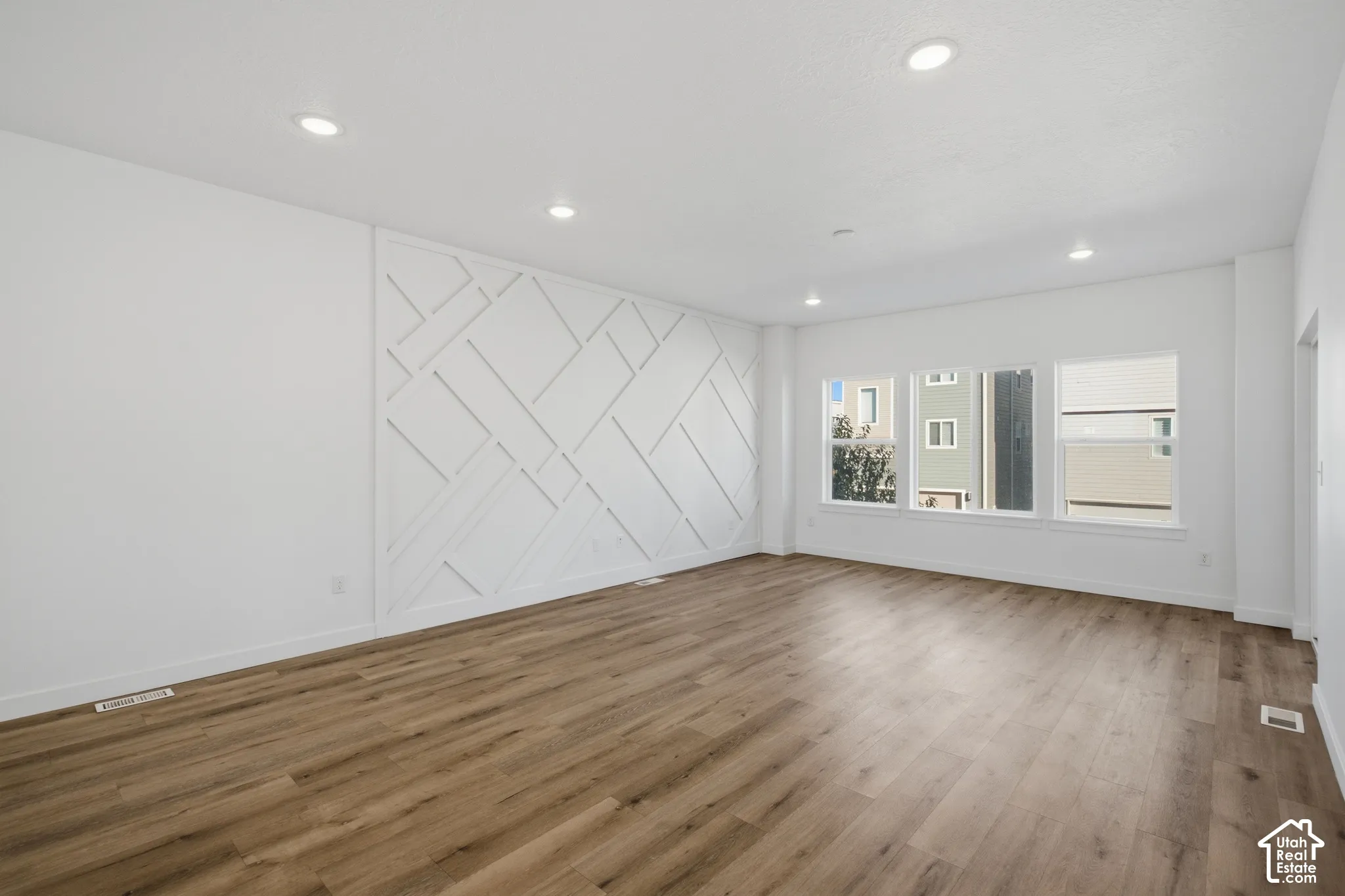 Spacious room featuring wood-finish flooring, decorative wall molding, recessed lighting, and large windows