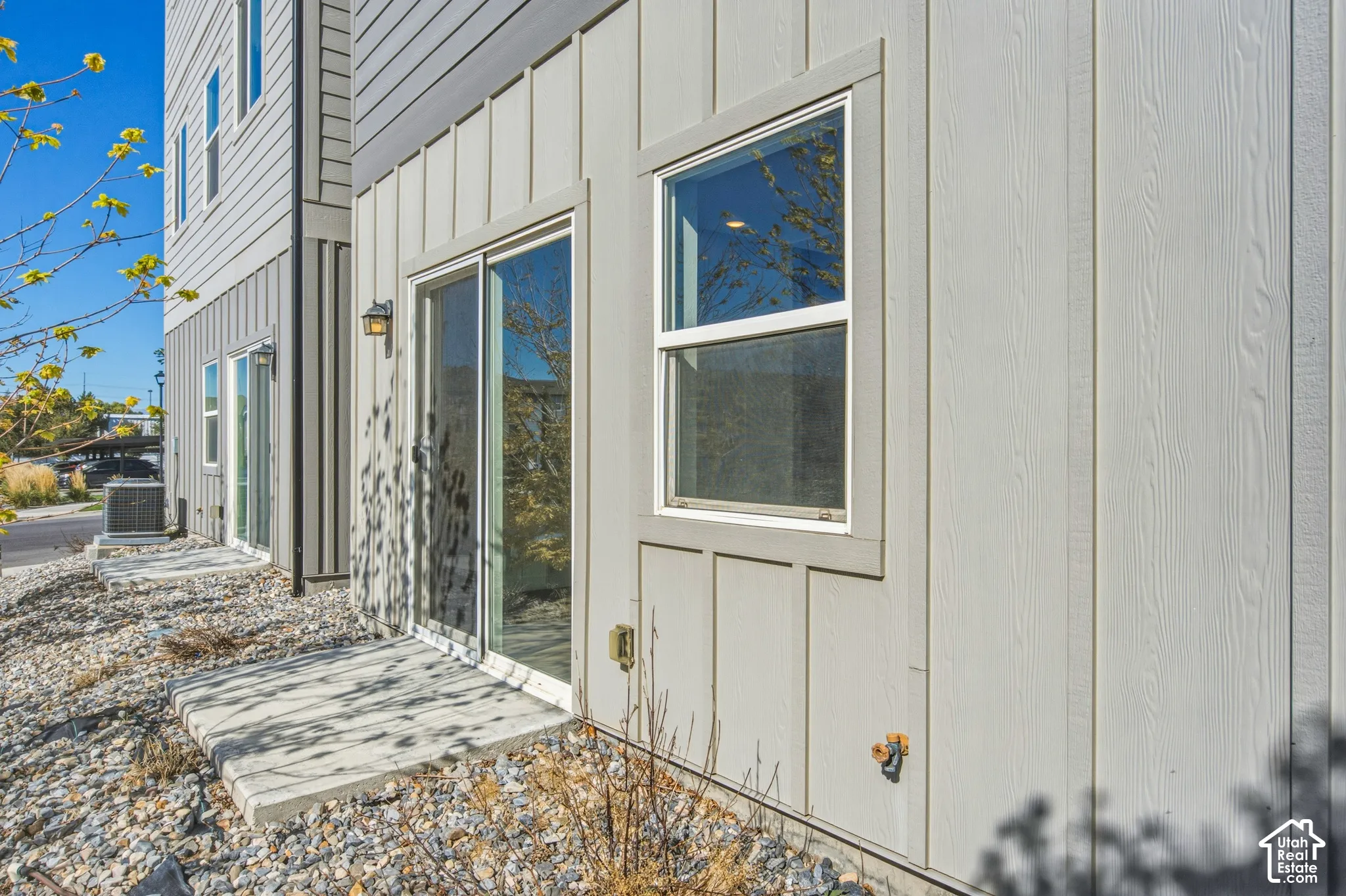 Exterior featuring vertical board-and-batten siding, concrete patio, sliding glass door, single-hung window, and wall-mounted exterior lighting