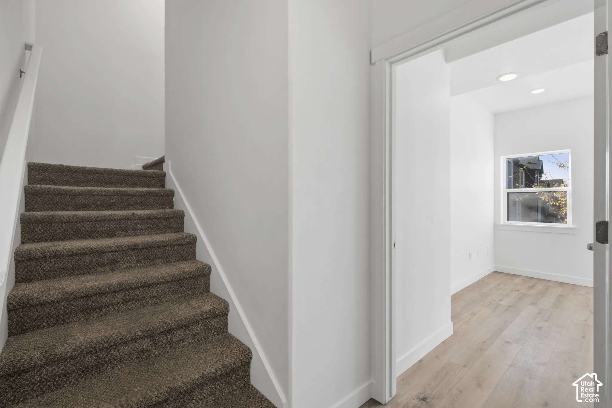 Staircase featuring wall-to-wall carpeting and a white handrail, paired with wood-finish flooring, recessed lighting, and a window with exterior exposure