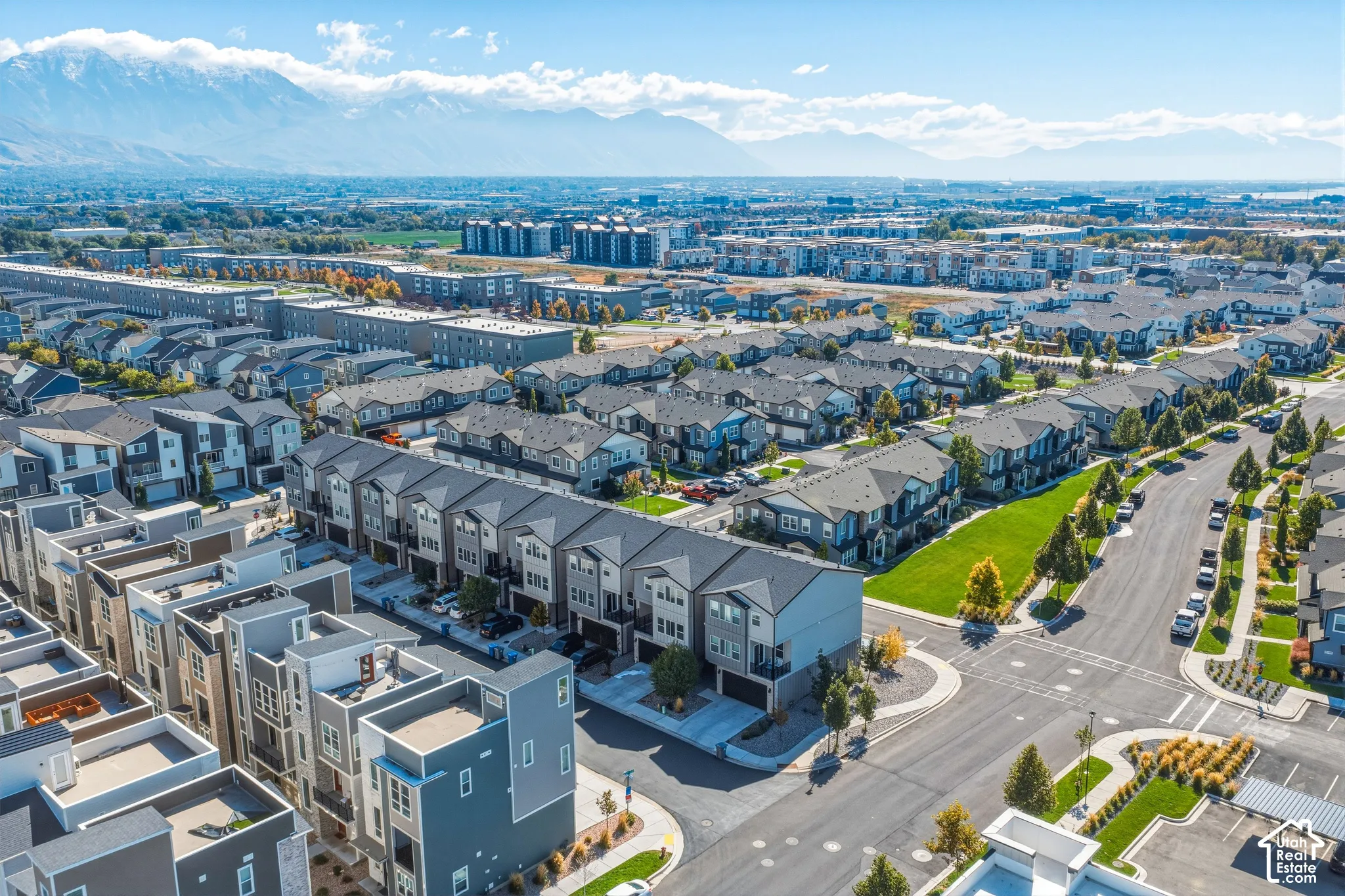Aerial perspective of residential community featuring mountain backdrops, multi-level townhome exteriors, paved street infrastructure, and manicured green spaces