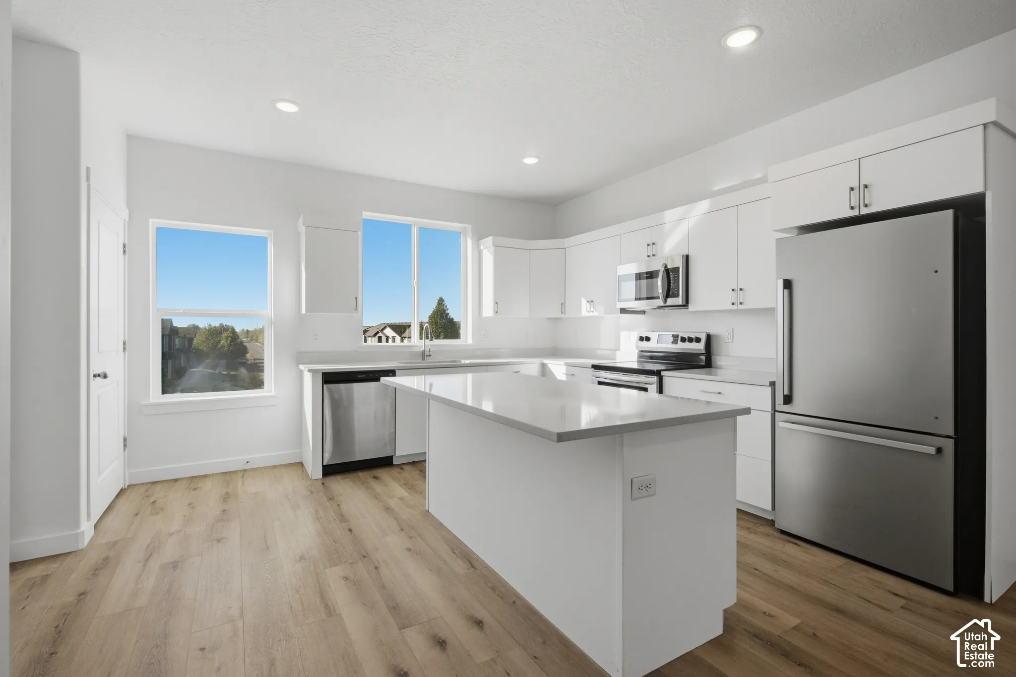 Kitchen featuring white cabinetry, quartz countertops, a central island, stainless steel appliances, and wood-finish flooring