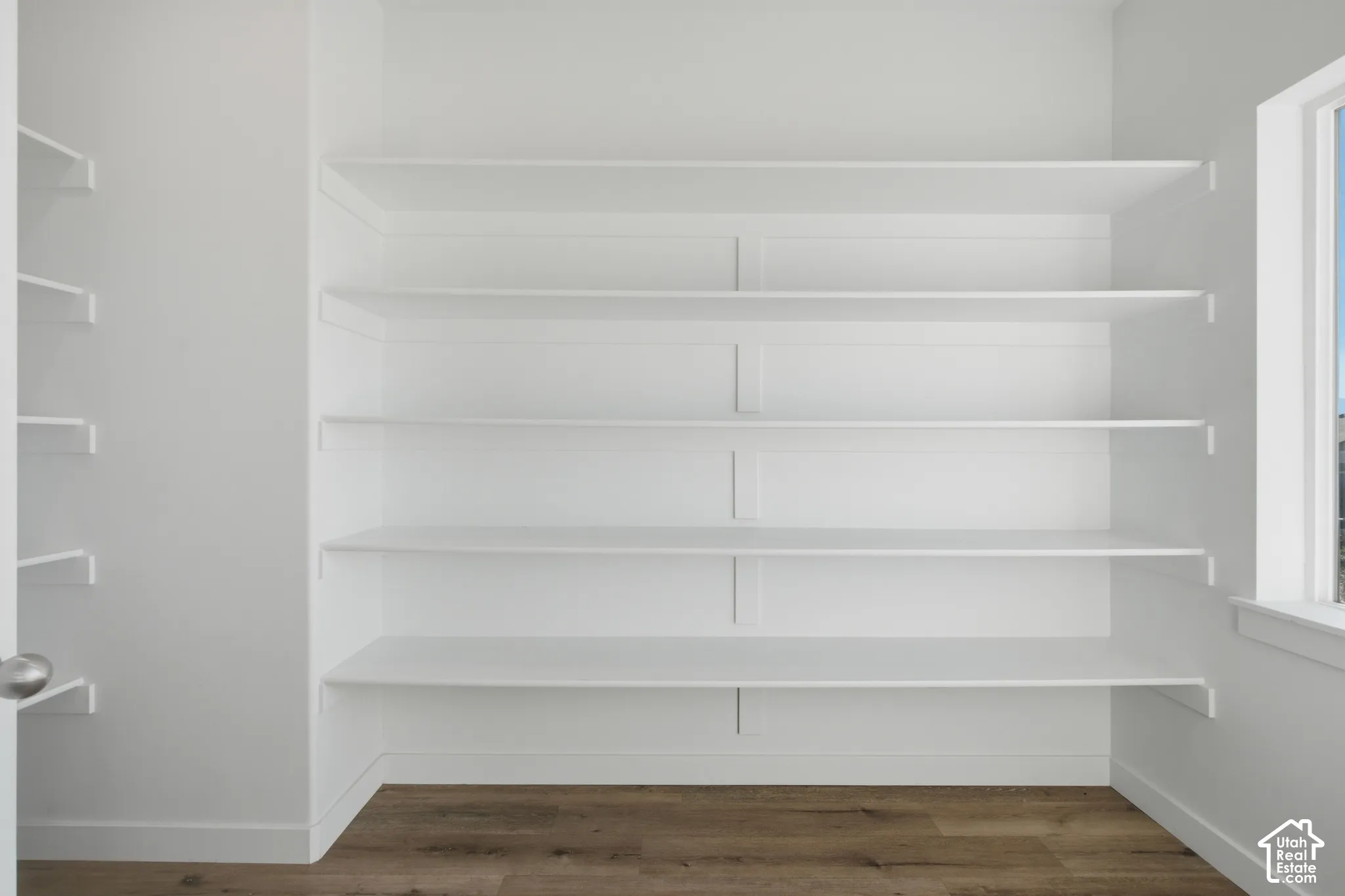 Built-in wall-to-wall shelving with a crisp finish, complemented by wood-finish flooring and a window providing natural light