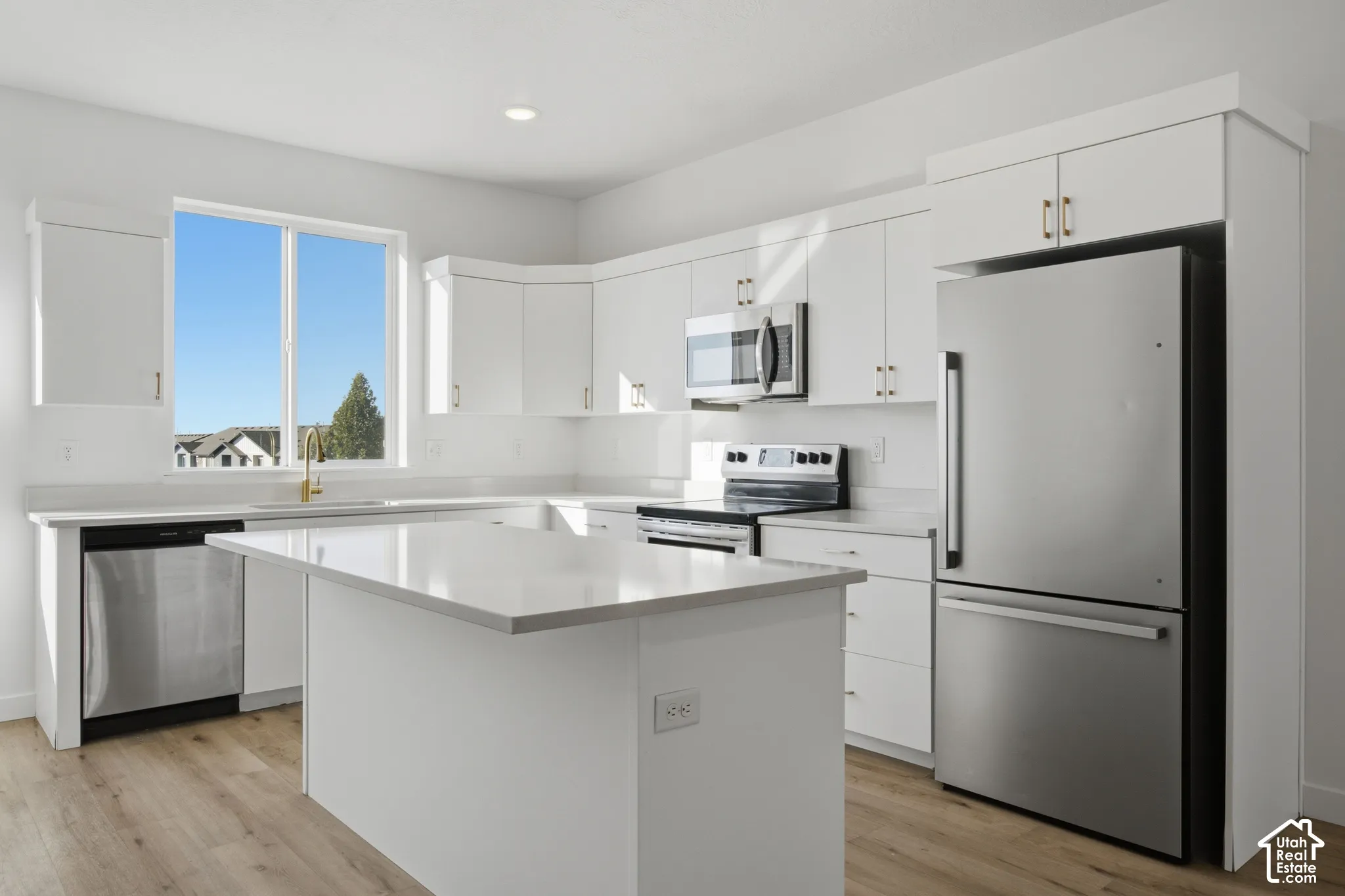 Kitchen featuring white cabinetry, an island with stone-finish countertops, wood-finish flooring, and stainless steel appliances