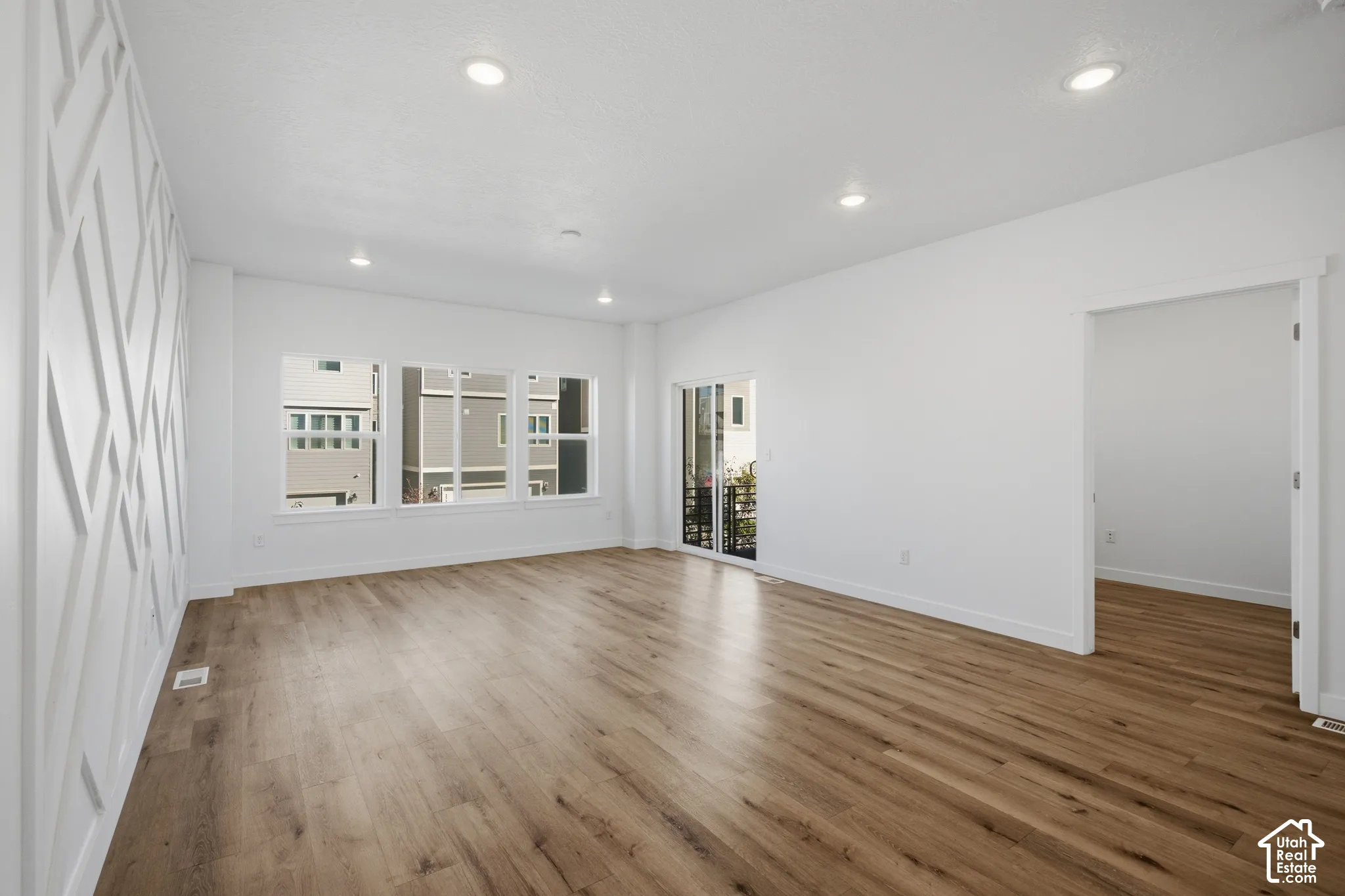 Living area featuring wood-finish flooring, recessed lighting, expansive windows, geometric wall molding, and sliding glass door access