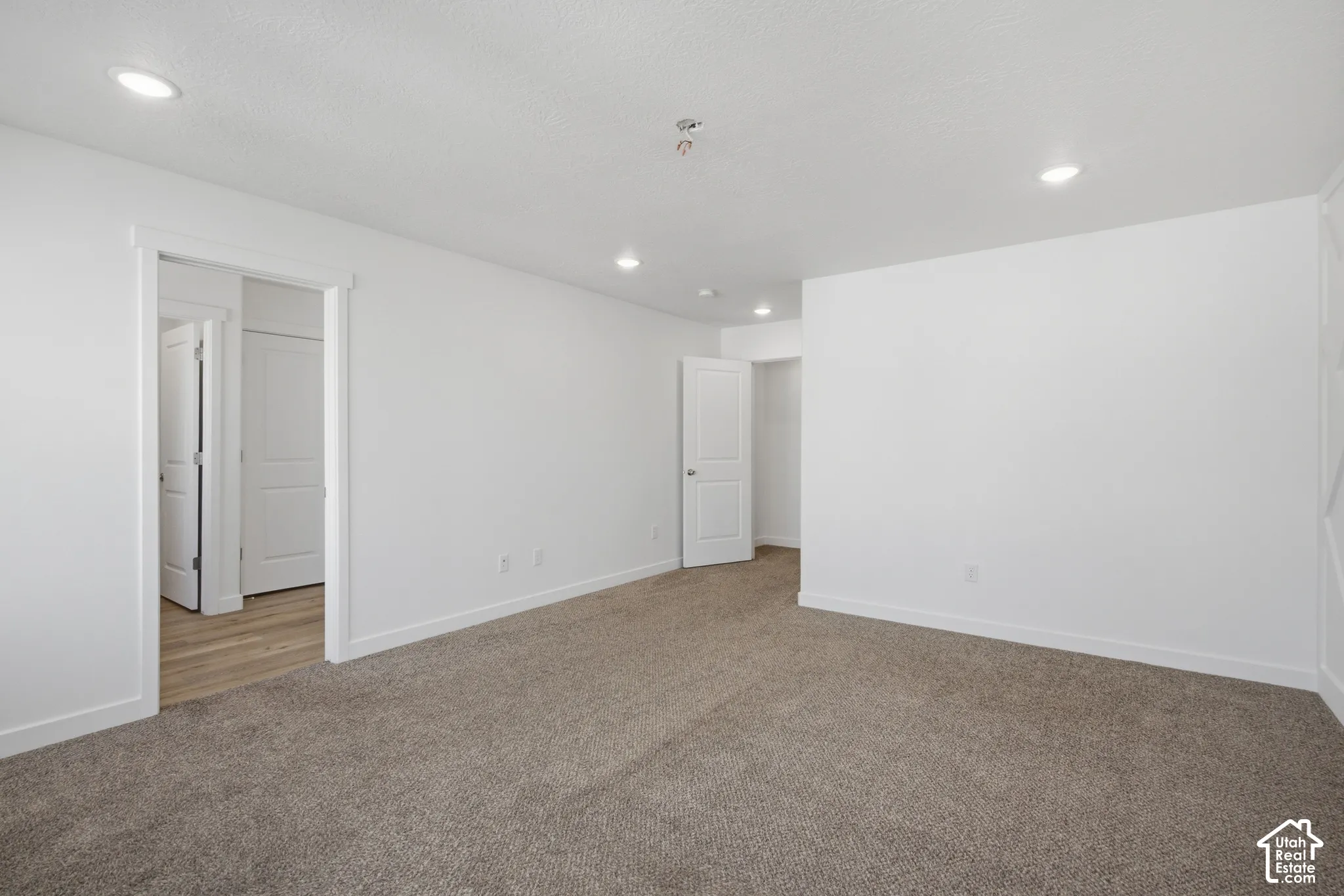 Neutral-toned carpeting, recessed ceiling lighting, and crisp white wall finishes featuring white-paneled interior doors
