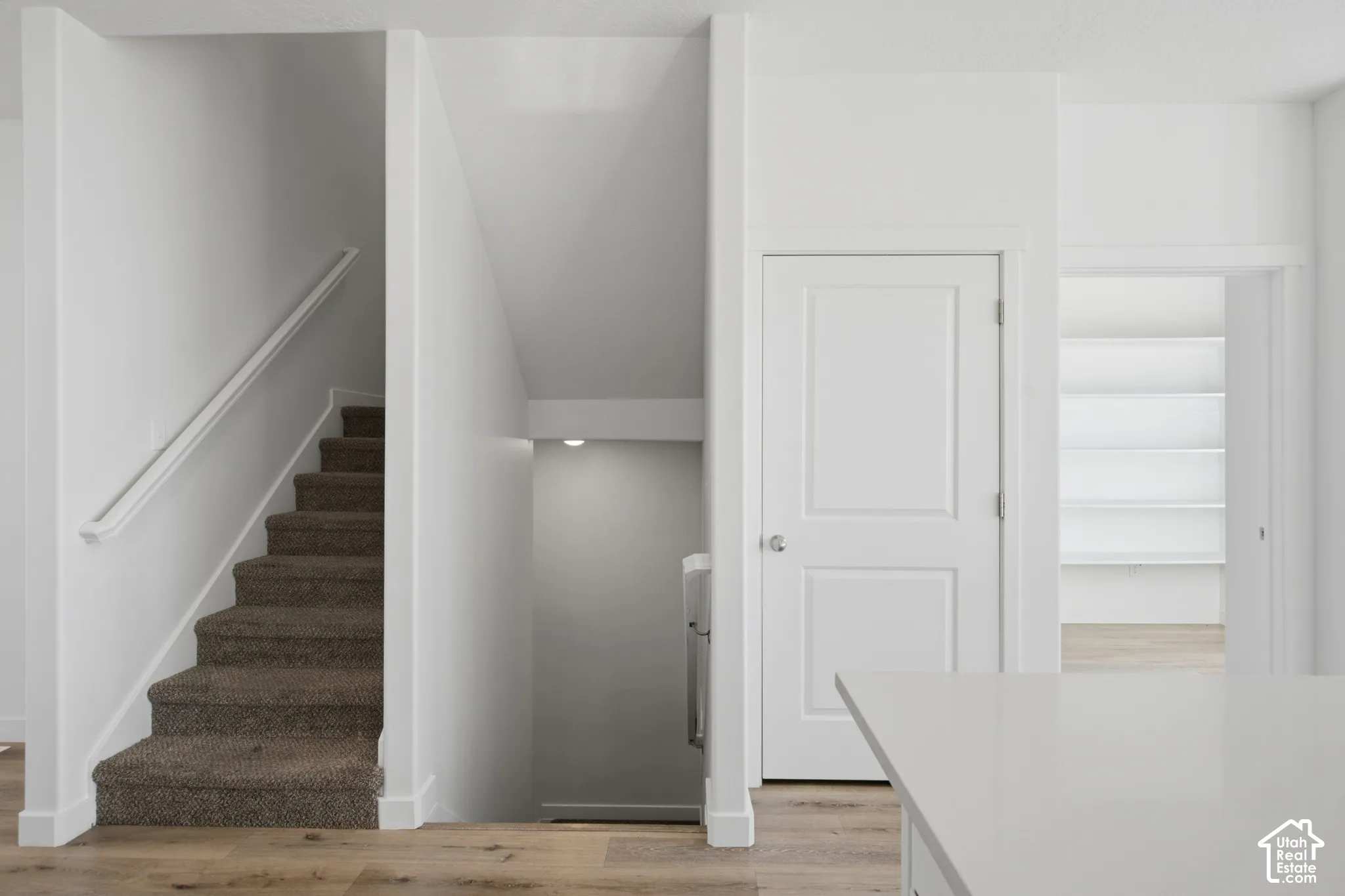 Staircase featuring carpeted treads, wall-mounted handrail, paneled interior door, and built-in wall shelving
