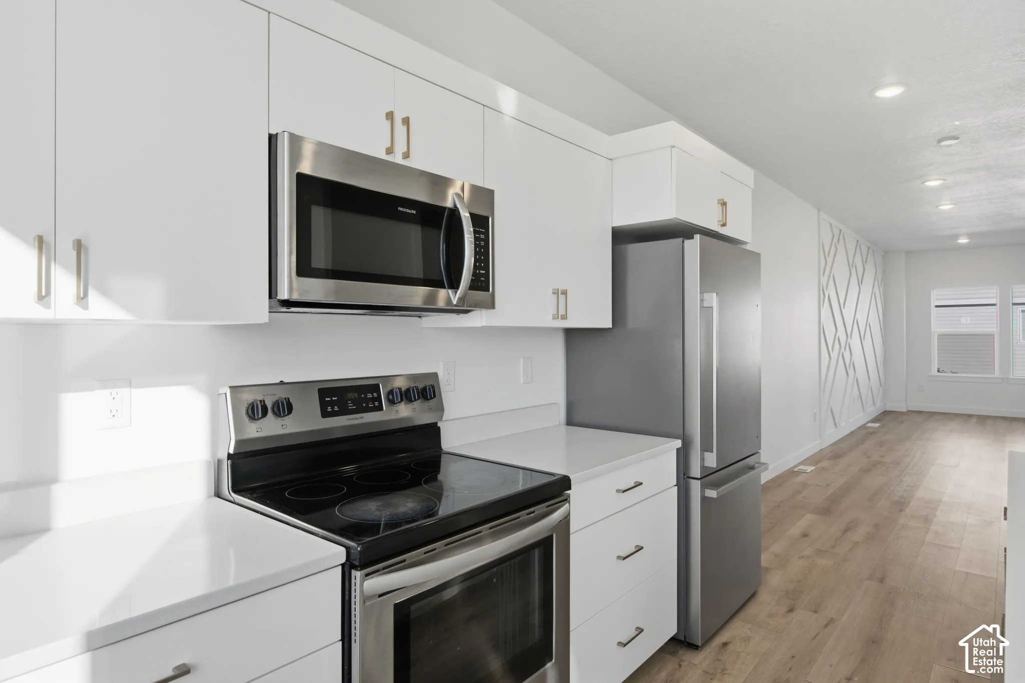 Kitchen featuring white flat-panel cabinetry, stainless steel appliances, quartz countertops, recessed lighting, and wood-finish flooring