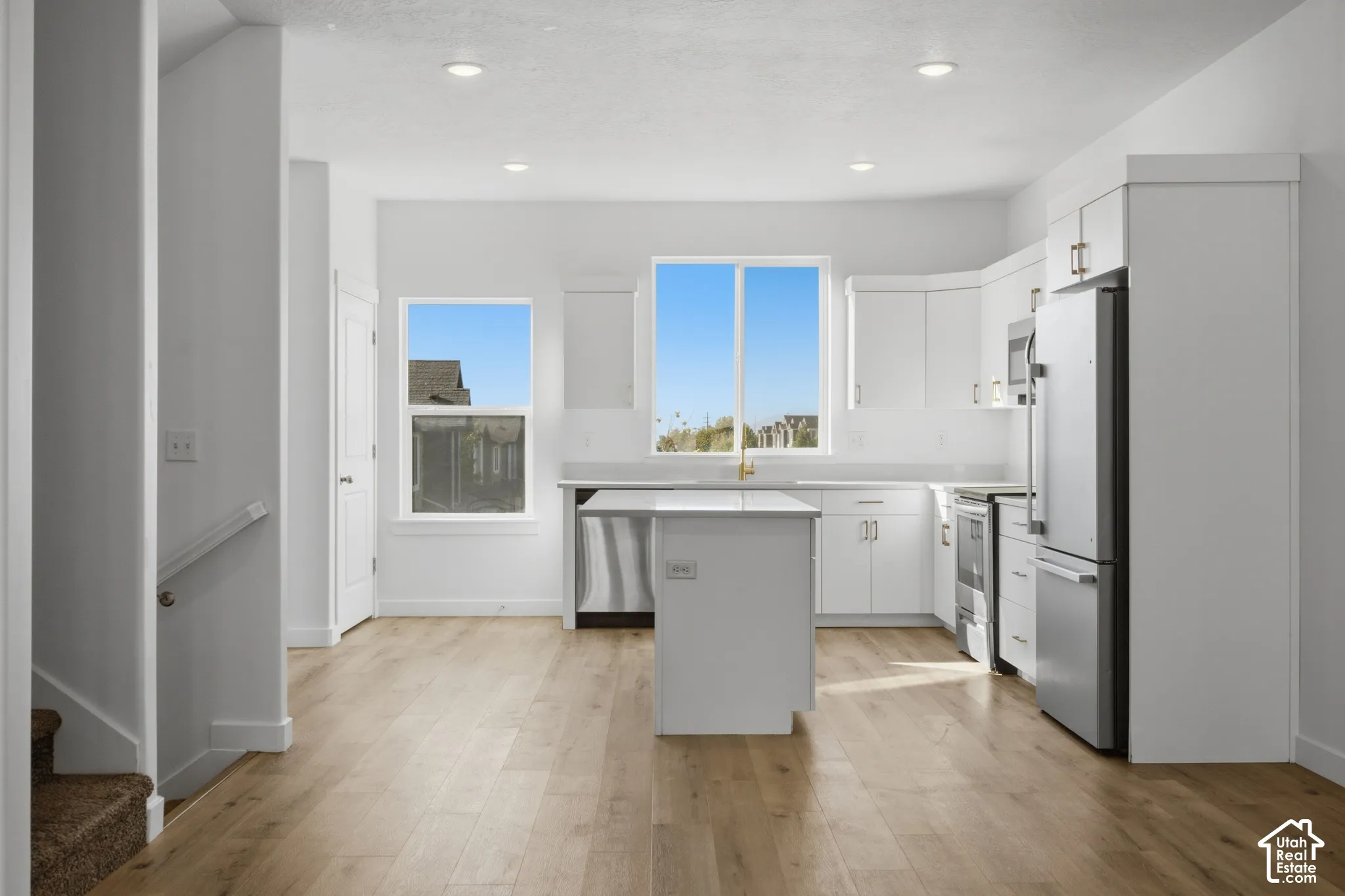Kitchen featuring white cabinetry, an island with stone-finish countertops, stainless steel appliances, and wood-finish flooring