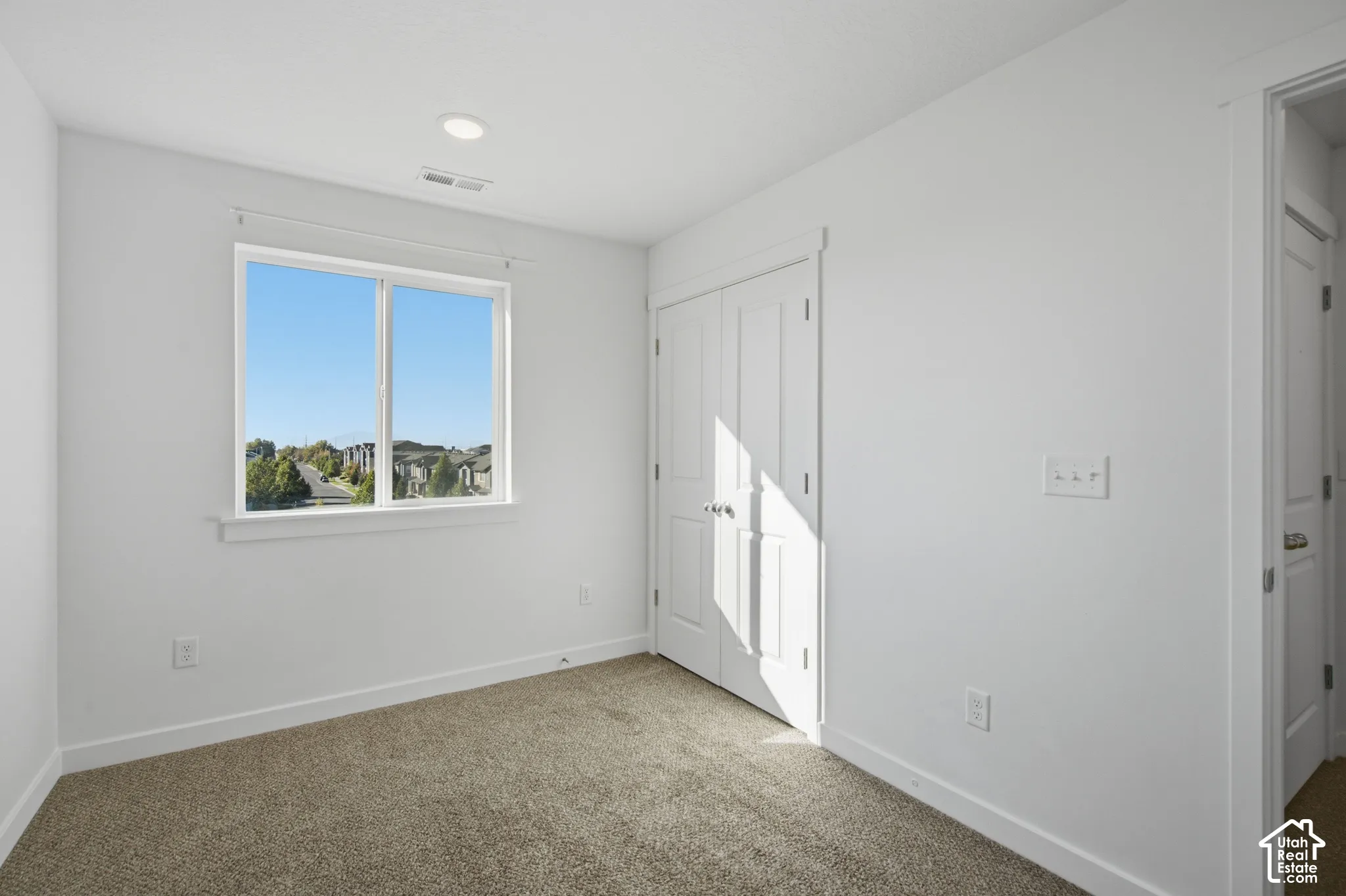 Neutral-toned wall-to-wall carpeting, single-hung window with exterior scenery, double-door closet with paneled detailing, and recessed ceiling lighting