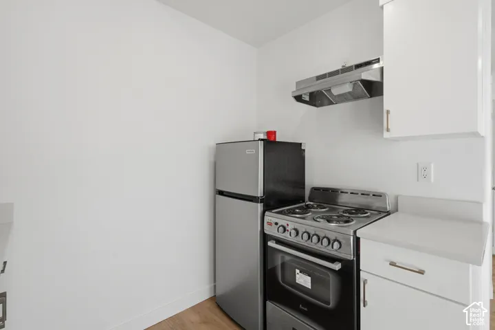 Compact kitchen area featuring white cabinetry, solid-surface countertops, a stainless steel gas range, a stainless steel refrigerator, and a wall-mounted stainless steel exhaust hood