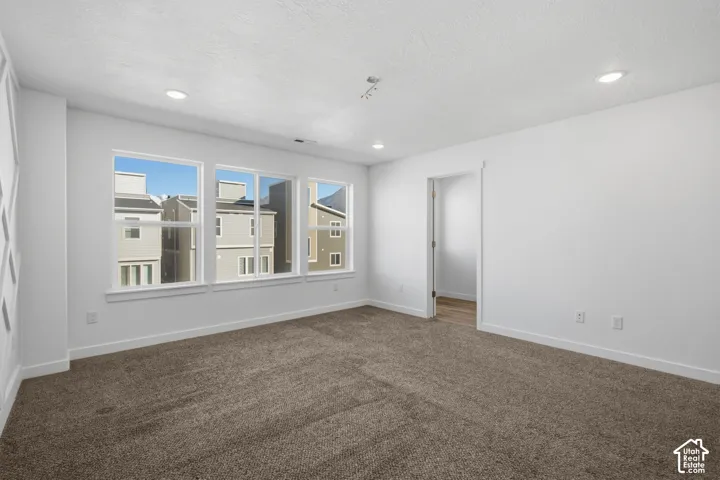 Neutral-toned interior room featuring wall-to-wall carpeting, recessed ceiling lighting, and a triple-window configuration with white trim