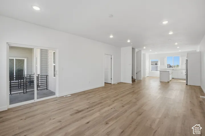 Open-concept living space featuring wood-finish flooring, recessed lighting, sliding glass door access to a balcony, and a kitchen equipped with a central island