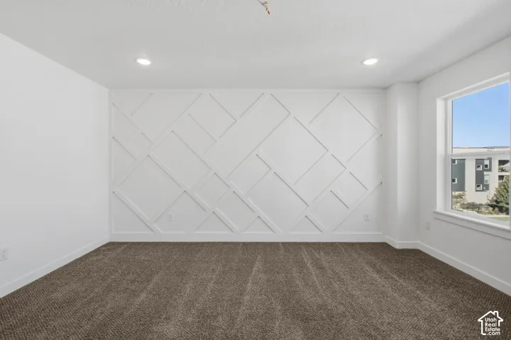 Geometric wall millwork, neutral carpeting, recessed ceiling lighting, and natural light from a single-pane window