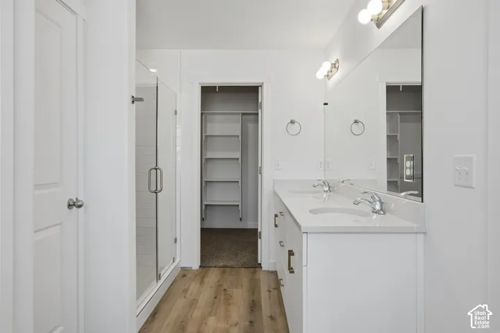 Dual-sink vanity with a solid-surface countertop, glass-enclosed shower, expansive wall-to-wall mirror, wood-finish flooring, and built-in closet shelving