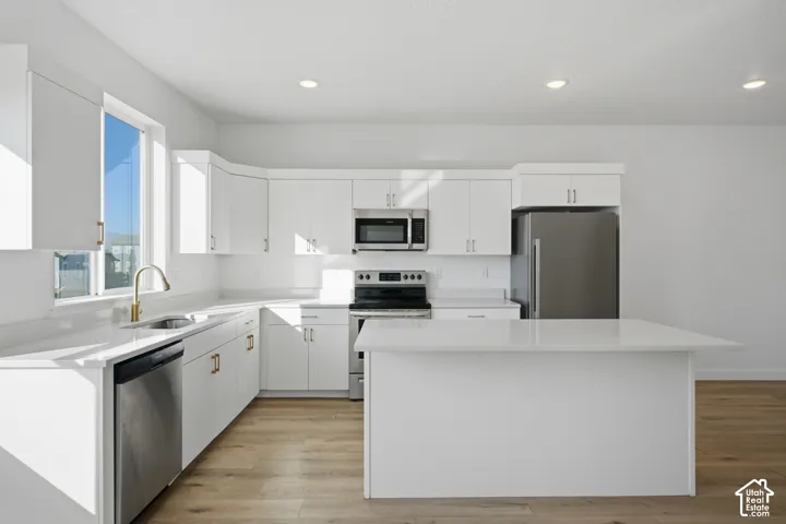 Kitchen featuring white cabinetry, quartz countertops, wood-finish flooring, a central island, and stainless steel appliances