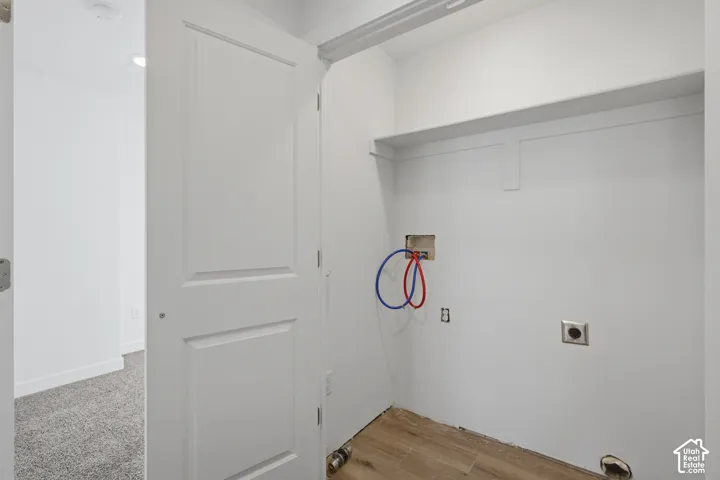 Utility alcove featuring wood-finish flooring, built-in shelving, and dedicated water and electrical hookups