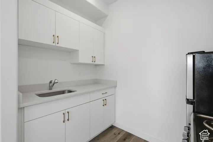 Utility space featuring white cabinetry with metallic pulls, stone-composite countertops, an undermount stainless steel sink, and wood-finish flooring