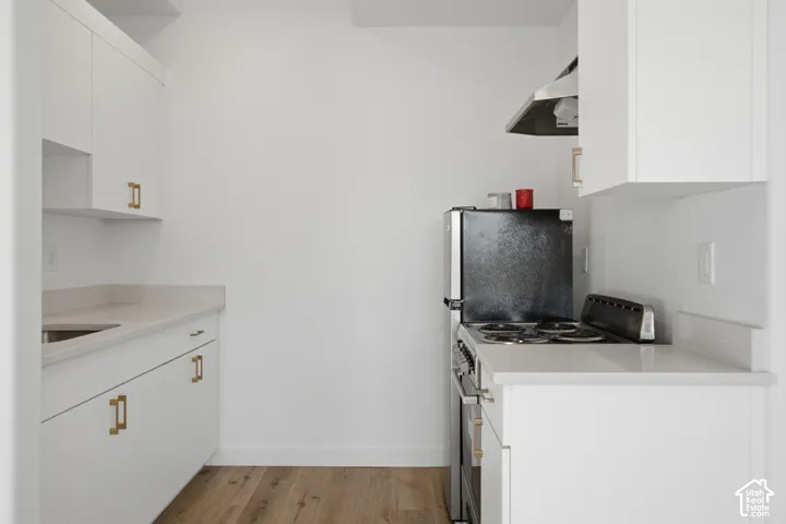 Kitchen featuring white cabinetry with brass-tone hardware, solid-surface countertops, wood-finish flooring, and a stainless steel range hood