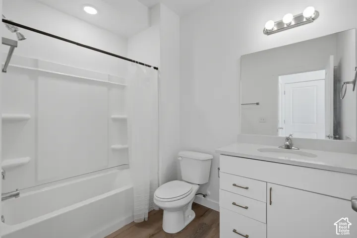 Bathroom featuring a white vanity with integrated countertop sink, wood-finish flooring, a tub-shower combination with built-in shelving, and polished chrome hardware