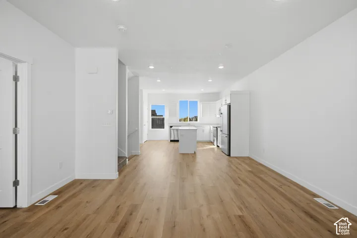 Open-concept floor plan featuring wood-finish flooring, recessed lighting, white cabinetry, a center island, and stainless steel appliances