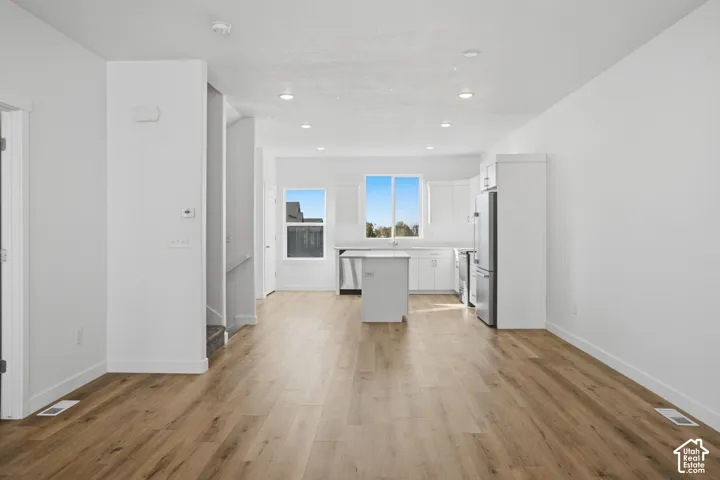 Open-concept interior featuring wood-finish flooring, white cabinetry, a central kitchen island, recessed lighting, and stainless steel appliances