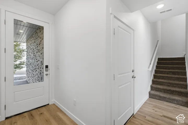 Entryway featuring a solid door with glass pane, recessed ceiling lighting, wood-finish flooring, and carpeted stairs with a white handrail