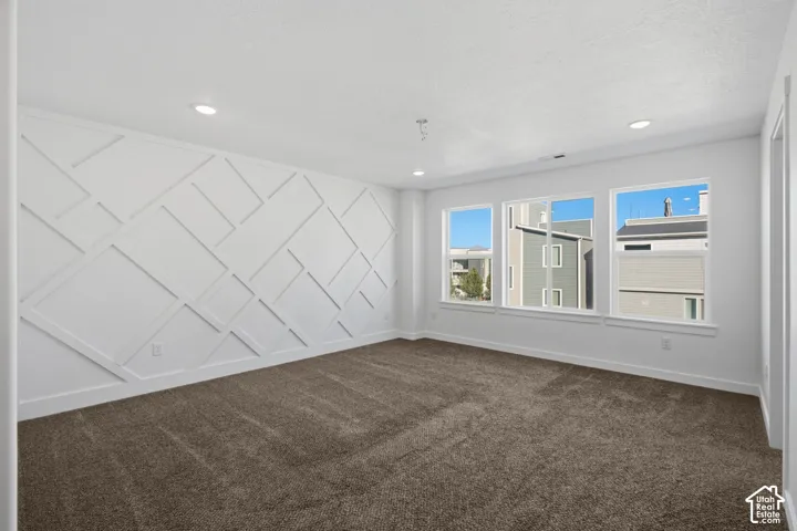 Room featuring a geometric wood wall accent, neutral carpeting, and multiple windows providing natural light, finished with recessed lighting