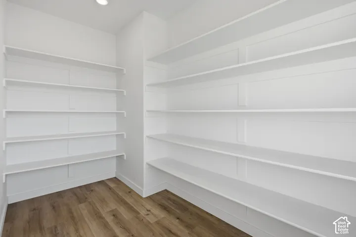 Walk-in storage area featuring floor-to-ceiling built-in white shelving, custom wall paneling, and wood-finish flooring
