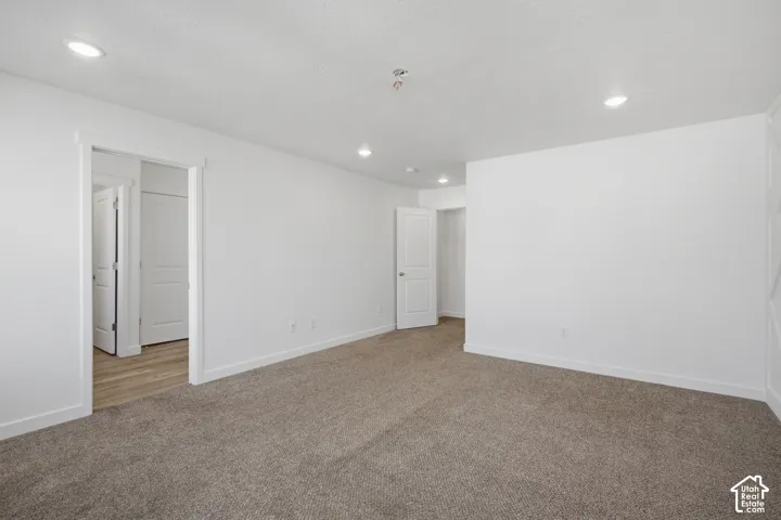 Neutral-toned carpeting, recessed ceiling lighting, and crisp white wall finishes featuring white-paneled interior doors